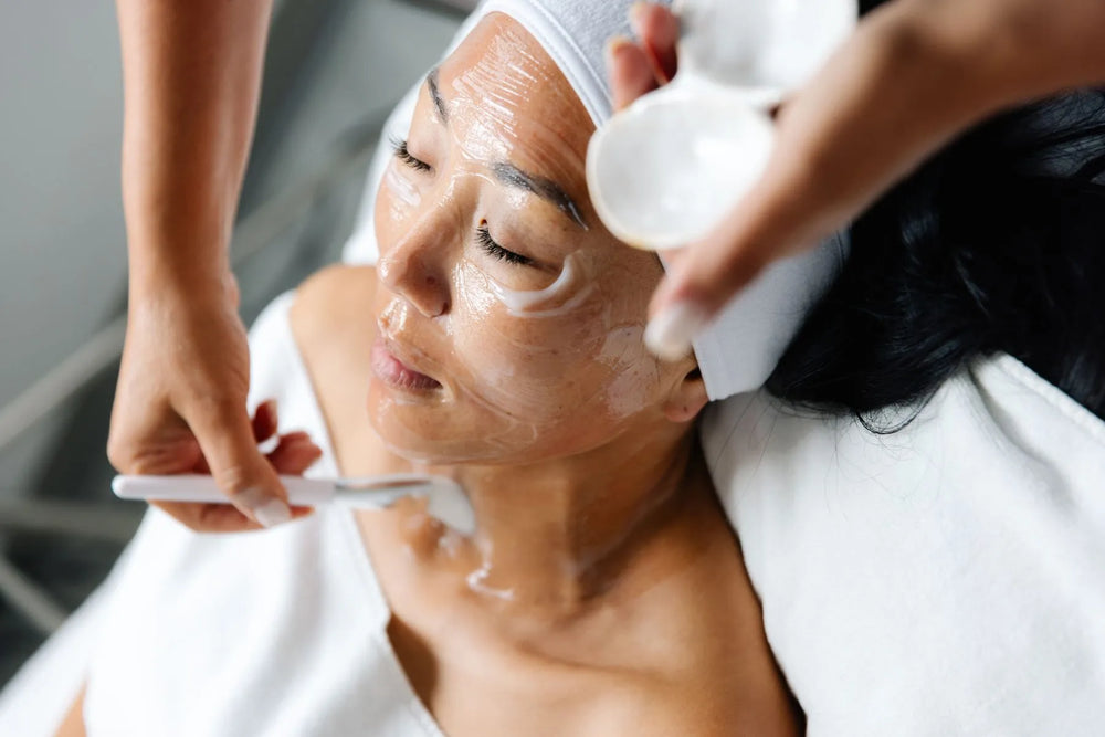 A professional esthetician gently applying a hydrating facial mask during a medical-grade facial treatment in Newport Beach